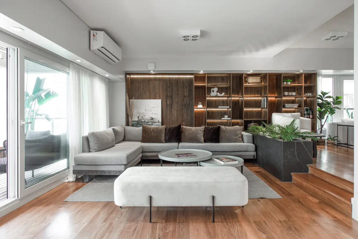 Sala de estar moderna com sofá modular cinza e prateleiras de madeira escura — projeto Depto Teodoro Garcia, por Ayelen Mayer Arquitectura, em Buenos Aires